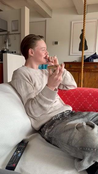 A person sitting on a couch in a living room, holding a phone